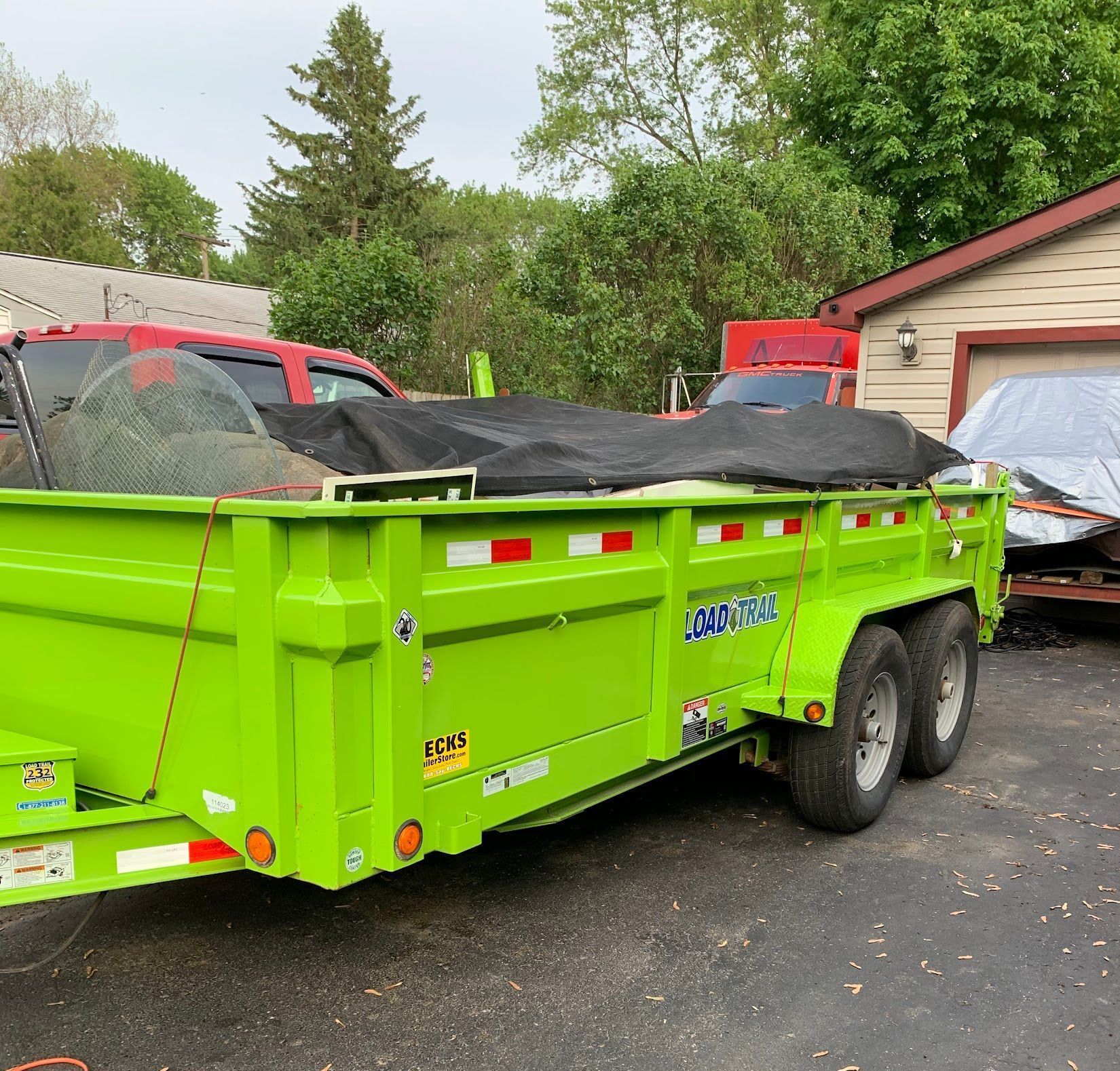 Bright green trailer loaded with debris, parked near a garage.