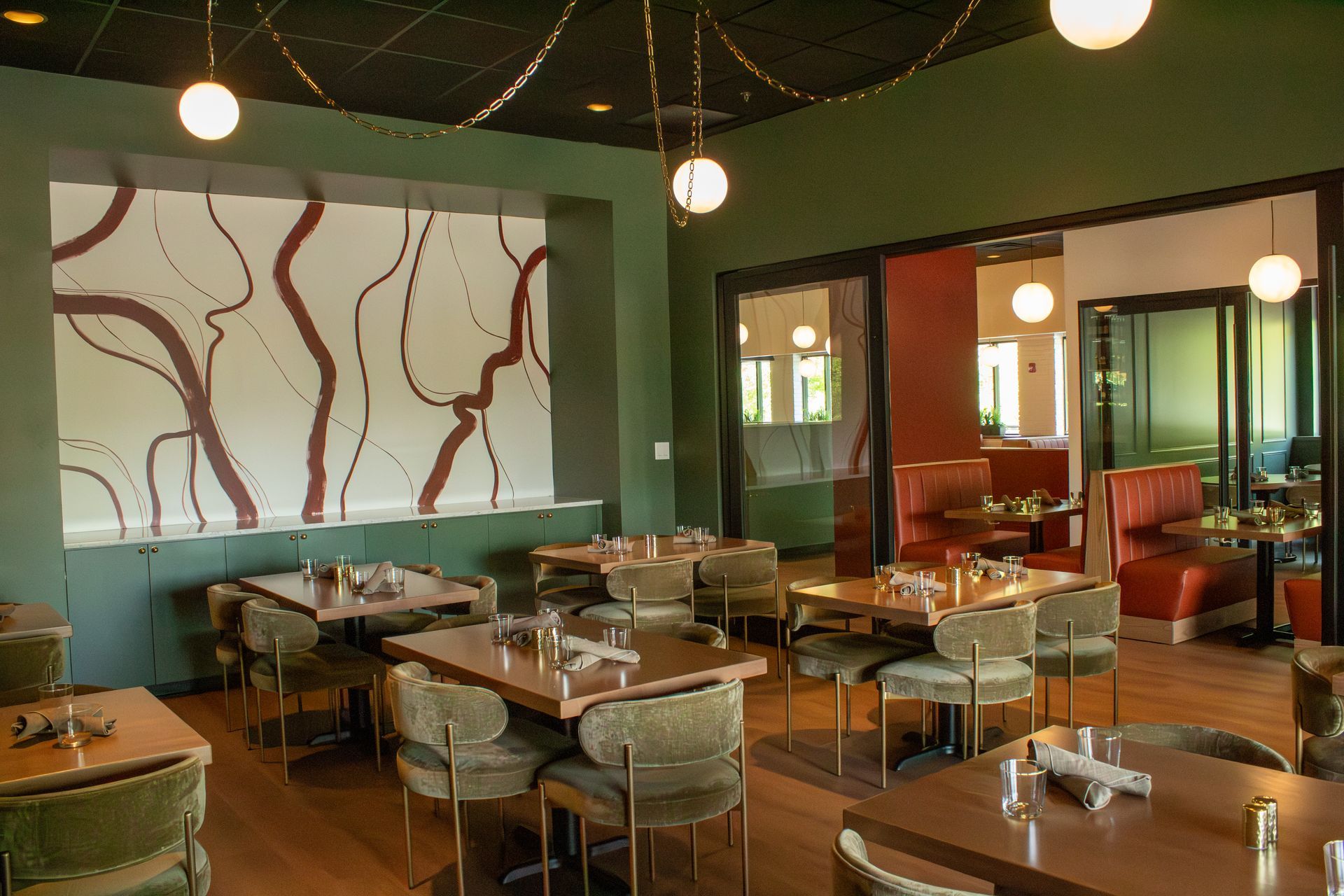 Empty restaurant dining room with teal walls, wooden tables, hanging lights, and abstract wall art