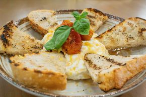 Plate of toast triangles with a poached egg, tomato sauce, and basil garnish