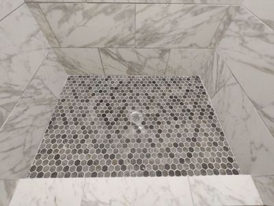 Shower floor with hexagonal mosaic tile and a central drain, surrounded by large marble-like tiles.