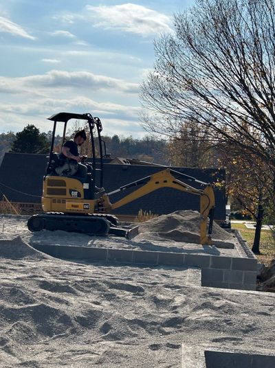 Excavator on a construction site; operator in the cab, moving gravel.