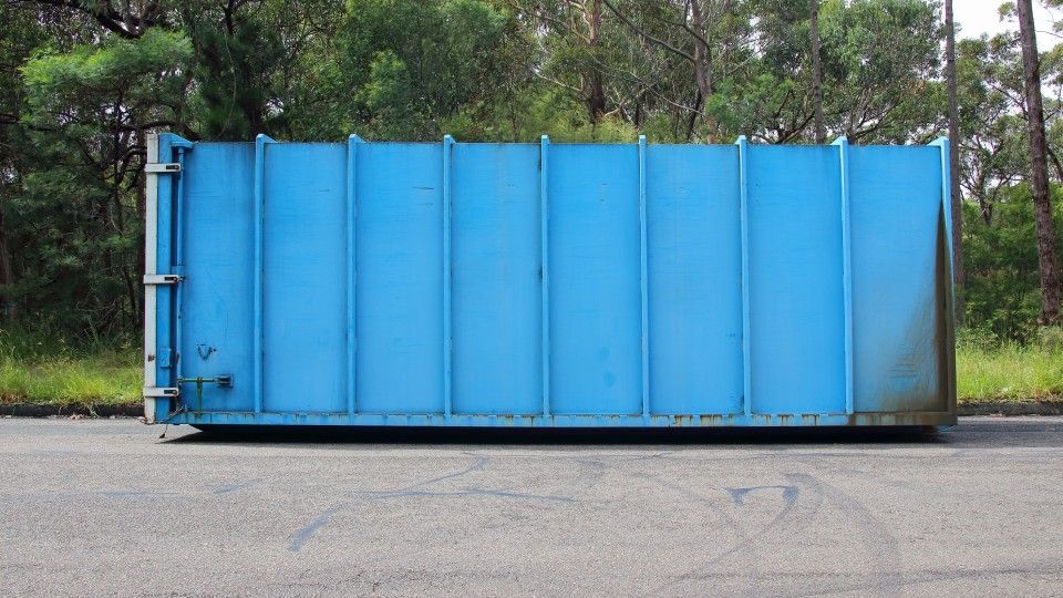 A blue dumpster is parked on the side of the road.