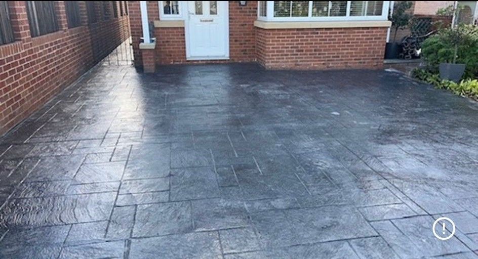 Wet stamped concrete driveway leading to a brick house with a white front door.