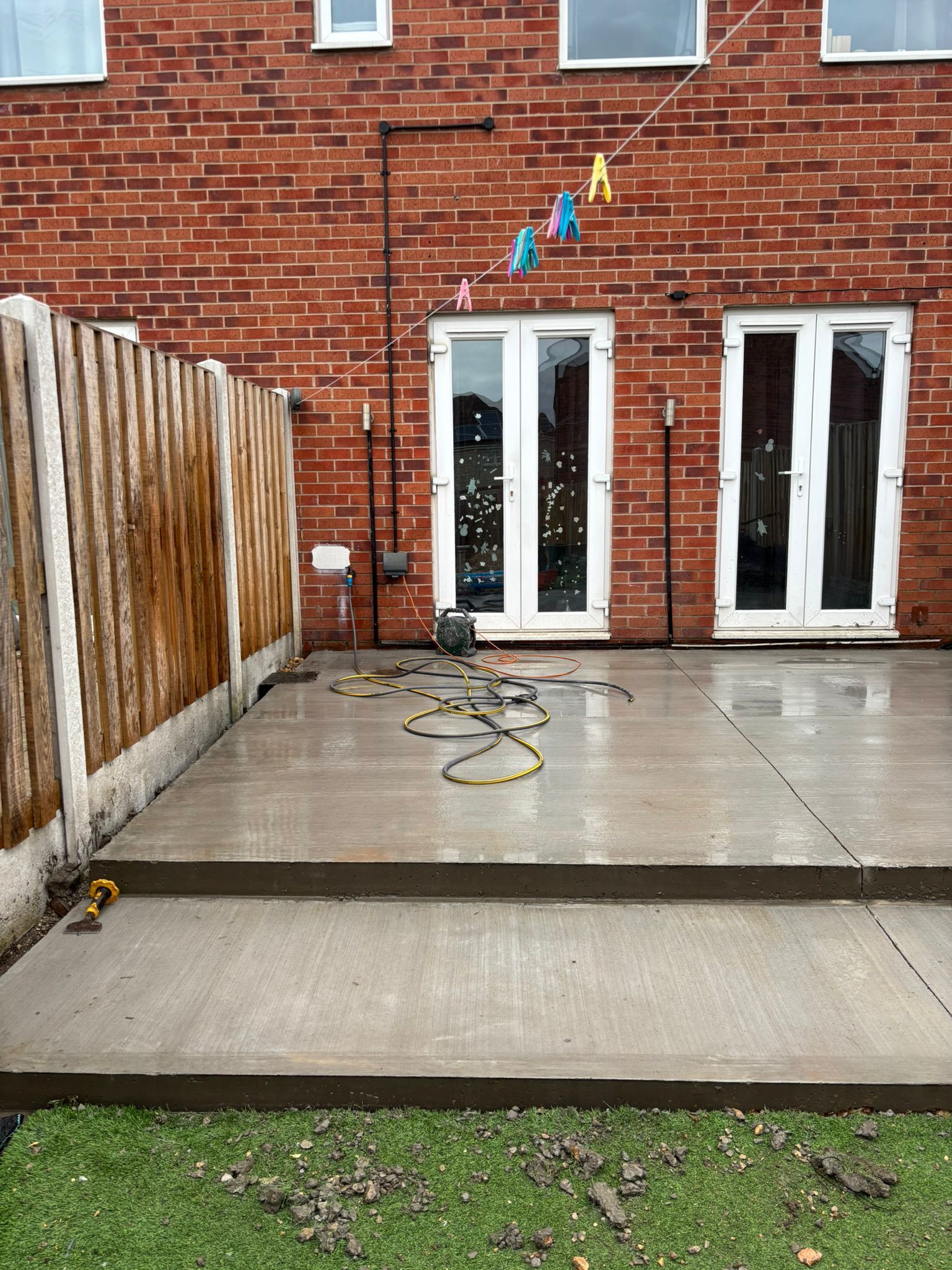 Wet backyard patio with brick house, glass doors, hose, and colorful bunting overhead