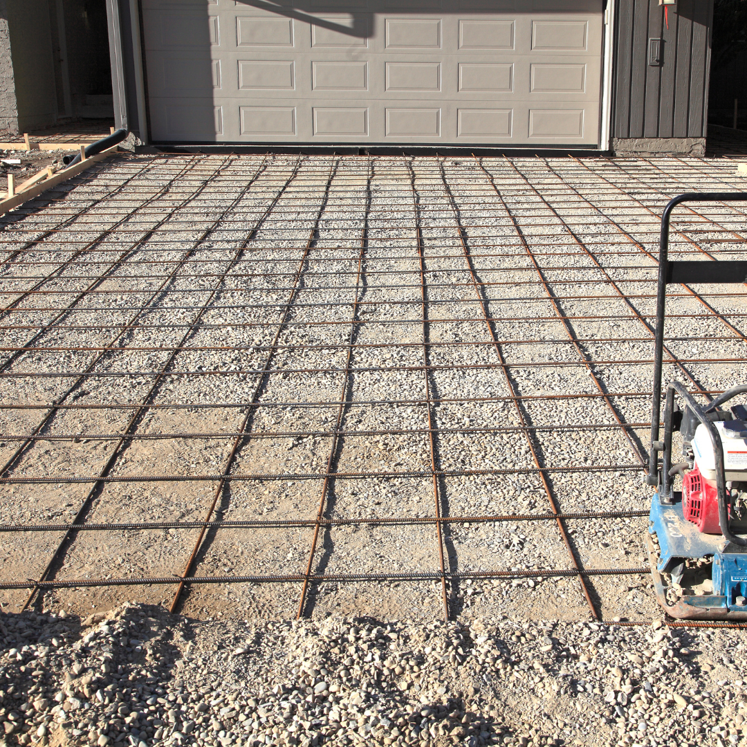 Rebar grid laid on a driveway foundation in front of a garage, with concrete gravel at the edge