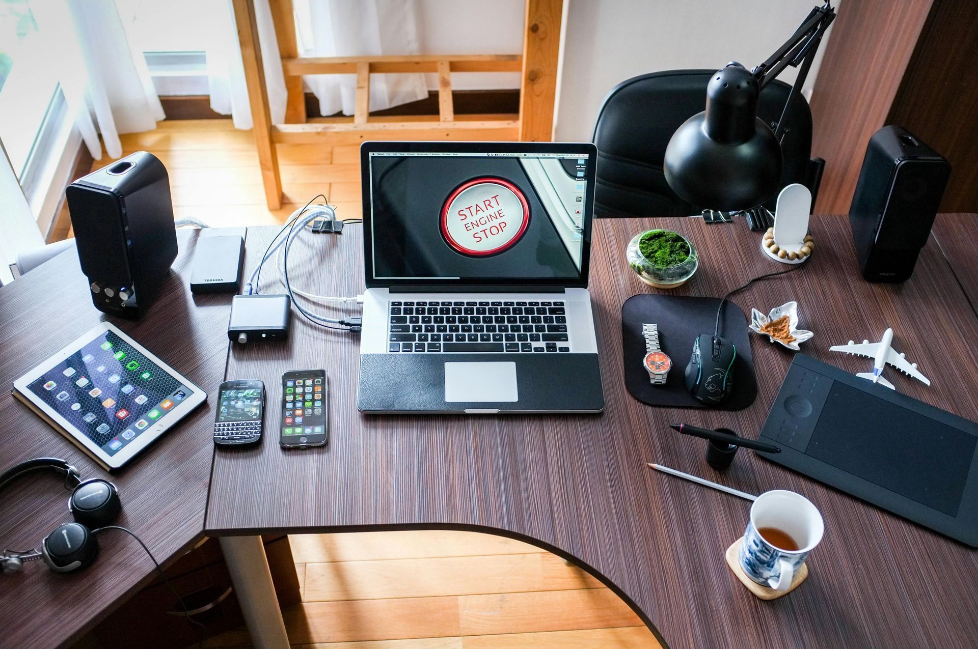 Laptop, tablet, and smartphone on a desk with speakers, accessories, and a small plant.