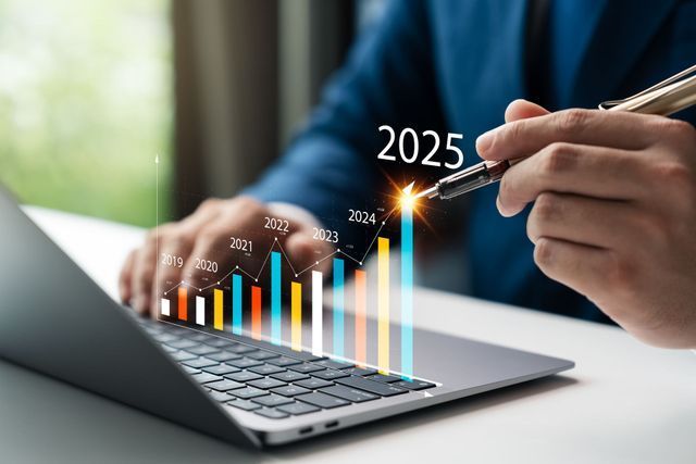 Person in suit pointing a pen at a rising bar graph on a laptop, labeled 2025.