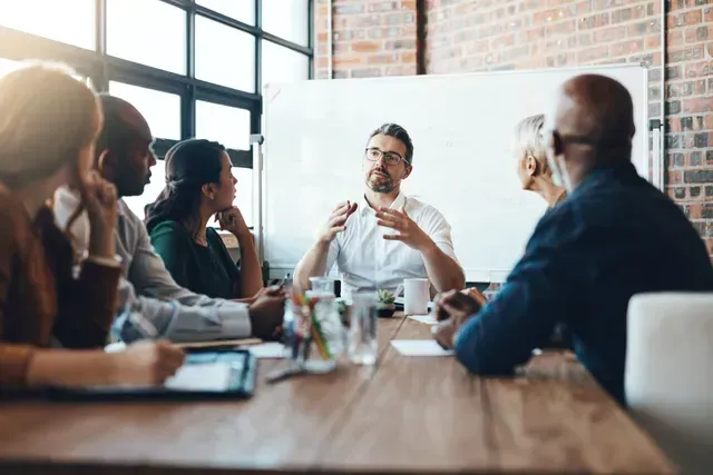 People in a meeting at a wooden table, discussing ideas in a bright office.
