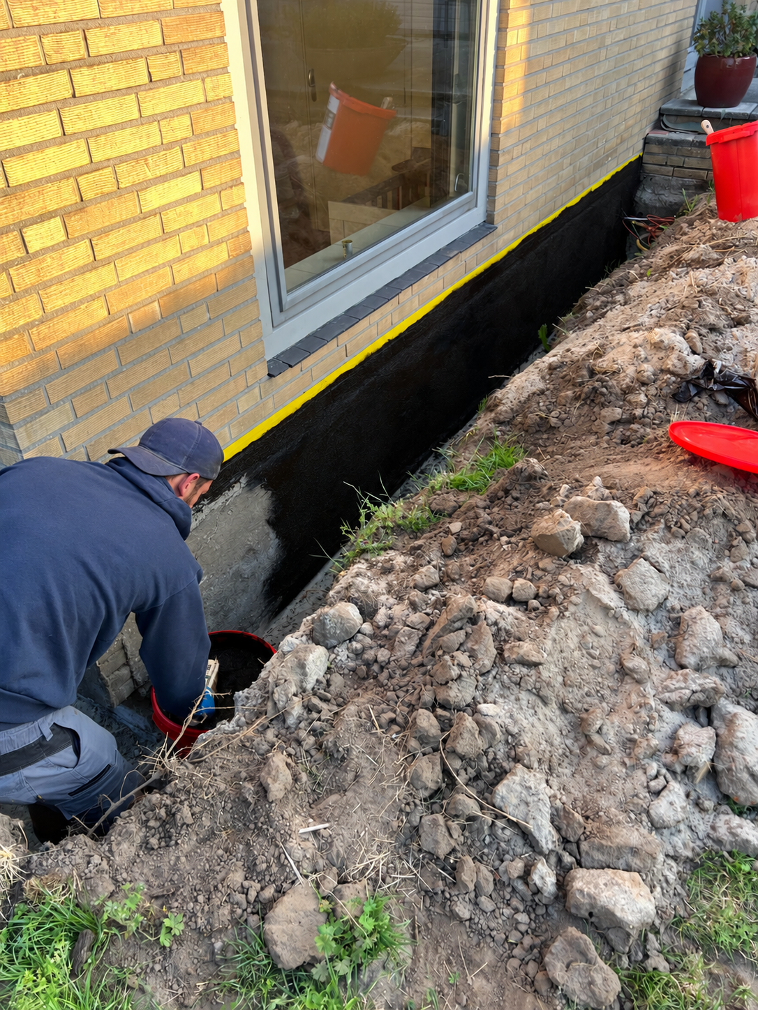 Een persoon reinigt met een hogedrukreiniger de bakstenen voorgevel van een huis; links op de foto is een ladder te zien.