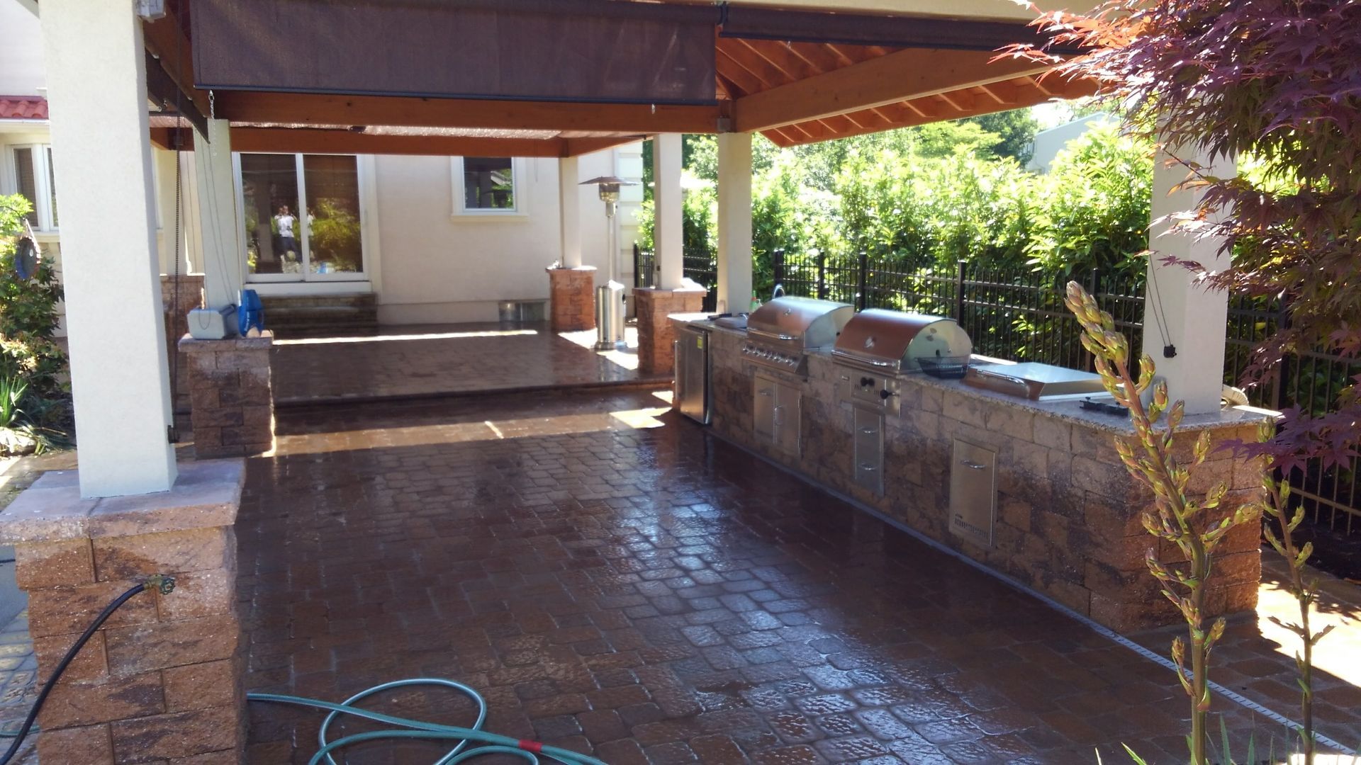 Covered patio with wet tiled floor, stone wall seating, and greenery in a courtyard