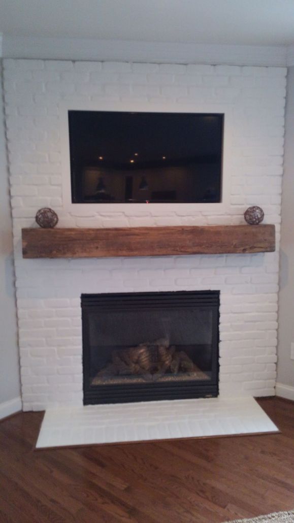 A white painted brick fireplace with a large wooden mantel, a wall-mounted TV, and a glass-front fireplace insert.
