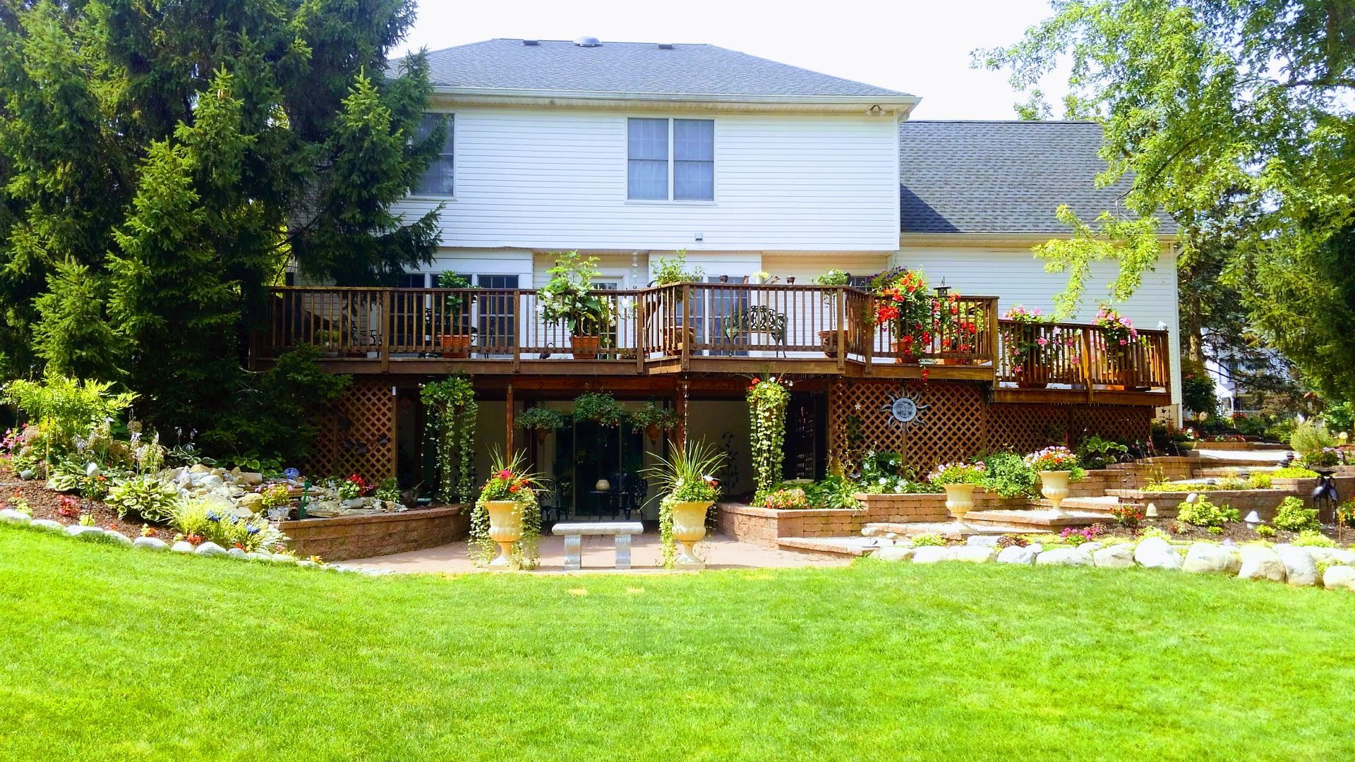 Two-story house with a wooden deck and lush green lawn in bright sunlight