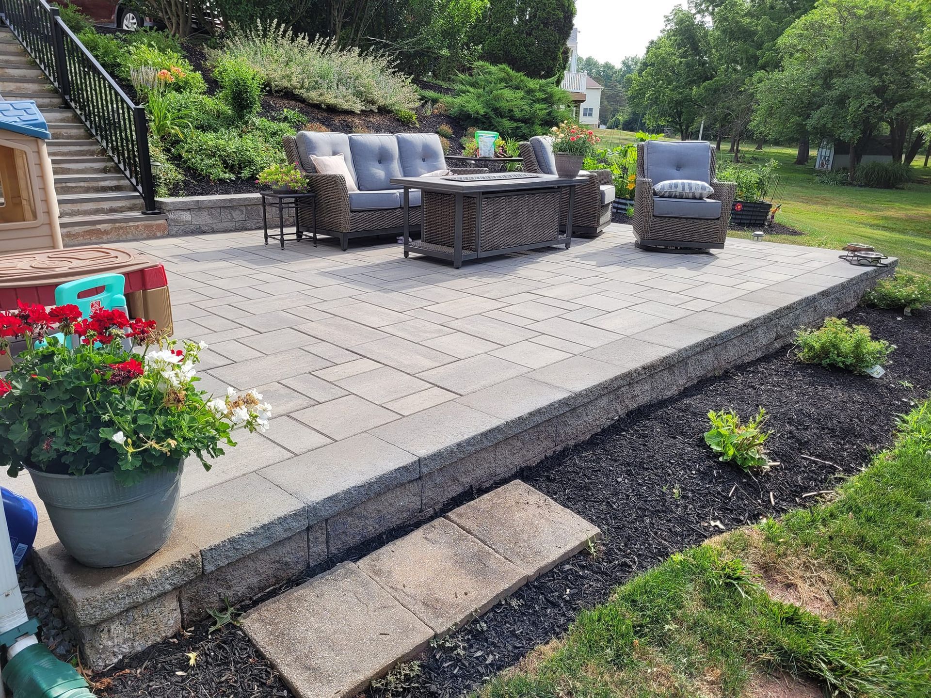 A patio with gray pavers featuring outdoor wicker furniture, a fire pit, and a flower pot in the foreground.
