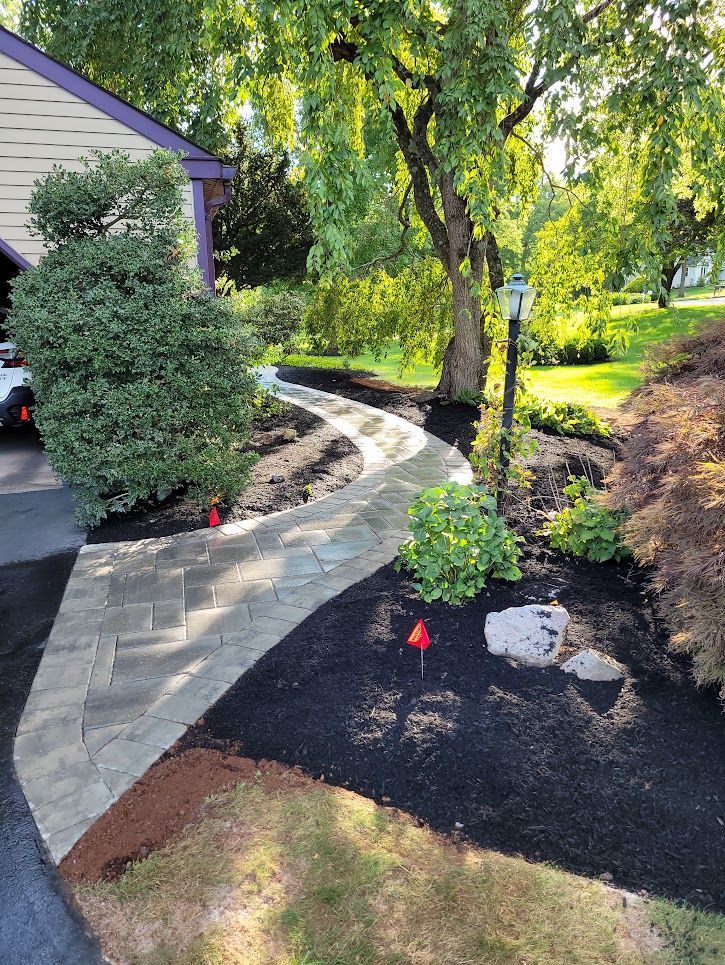 Curved concrete walkway beside a house and garden, with fresh black mulch and red markers under trees