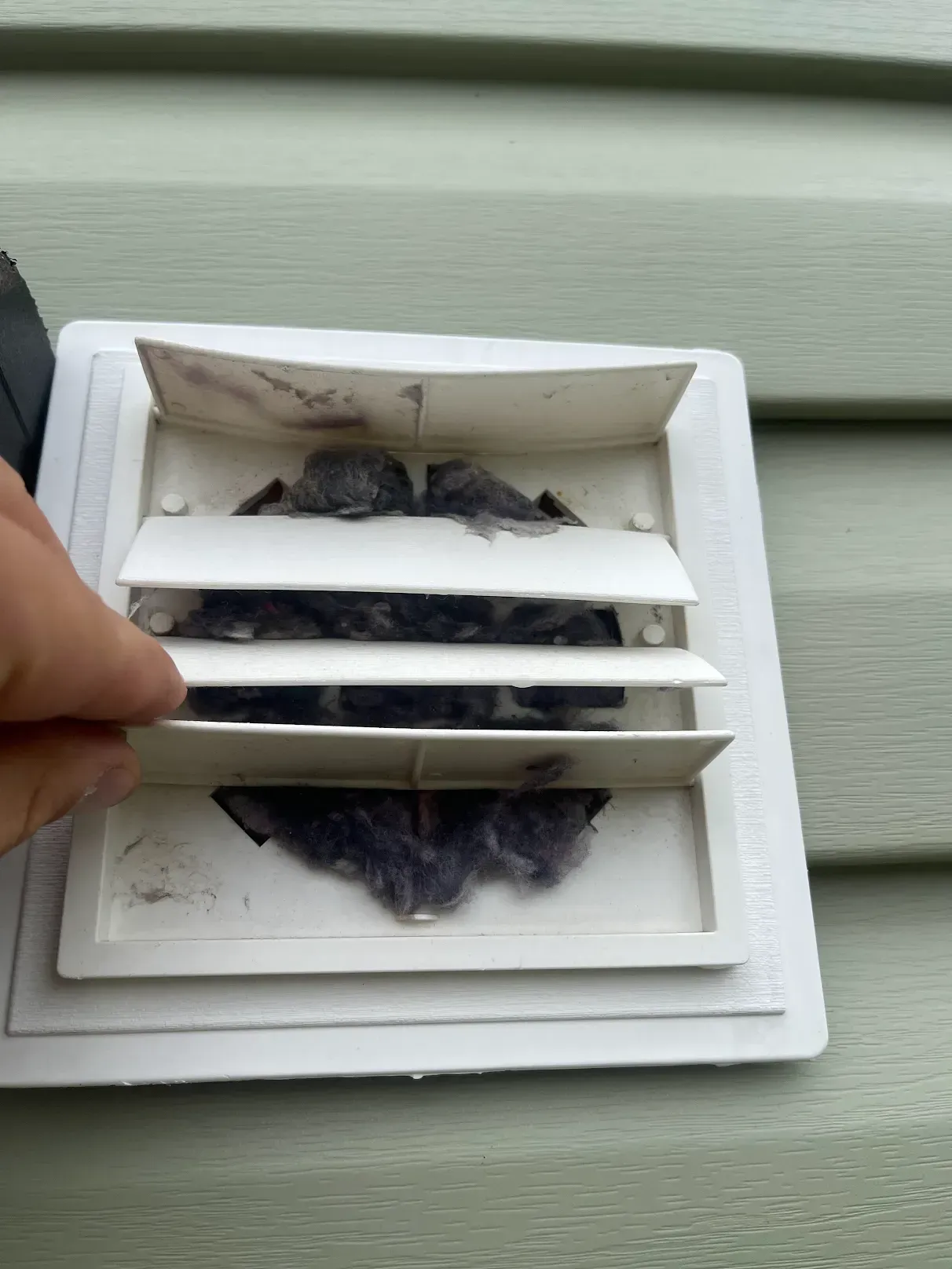 A person is cleaning a vent on the side of a house.