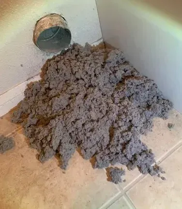 A pile of dust is sitting on the floor next to a duct.