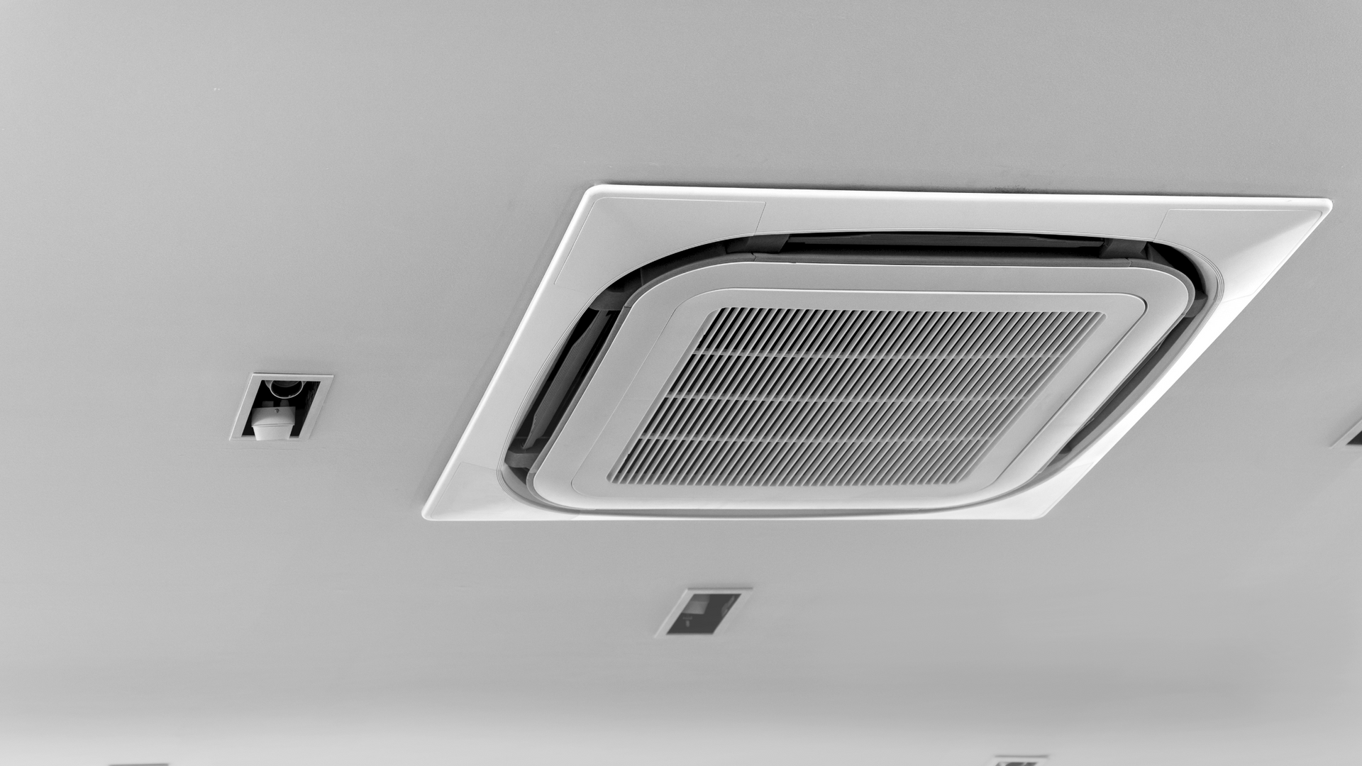 A black and white photo of a square air conditioner on the ceiling.