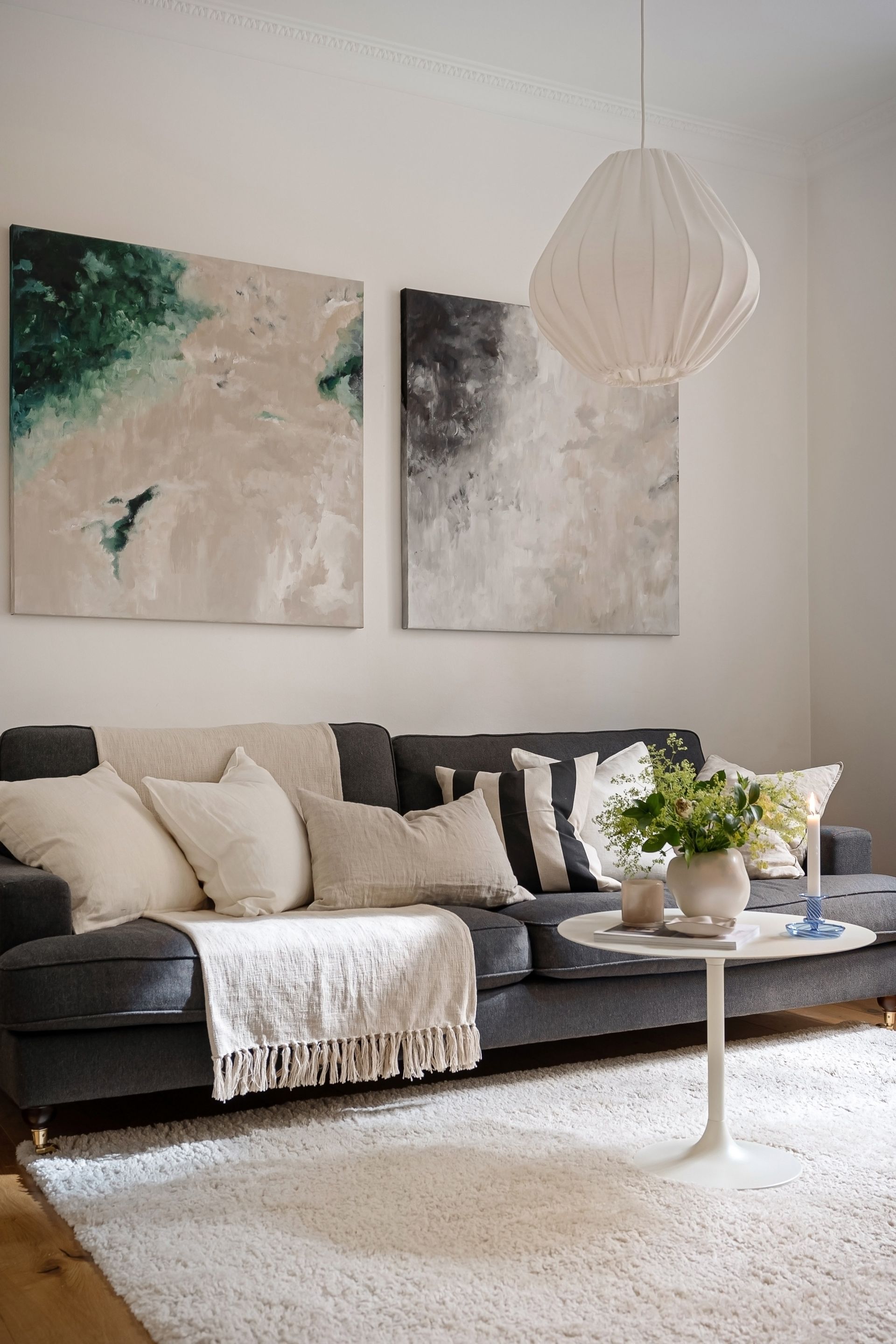 Un soggiorno moderno con un divano grigio scuro, cuscini decorativi chiari, opere d'arte astratte e un tavolino rotondo.