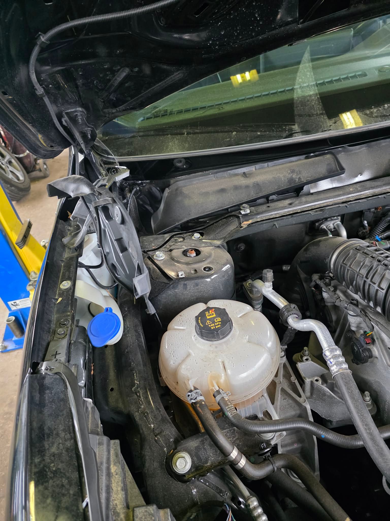 Black car engine bay with coolant reservoir and other components. Hood is open. | Seth's Auto Care