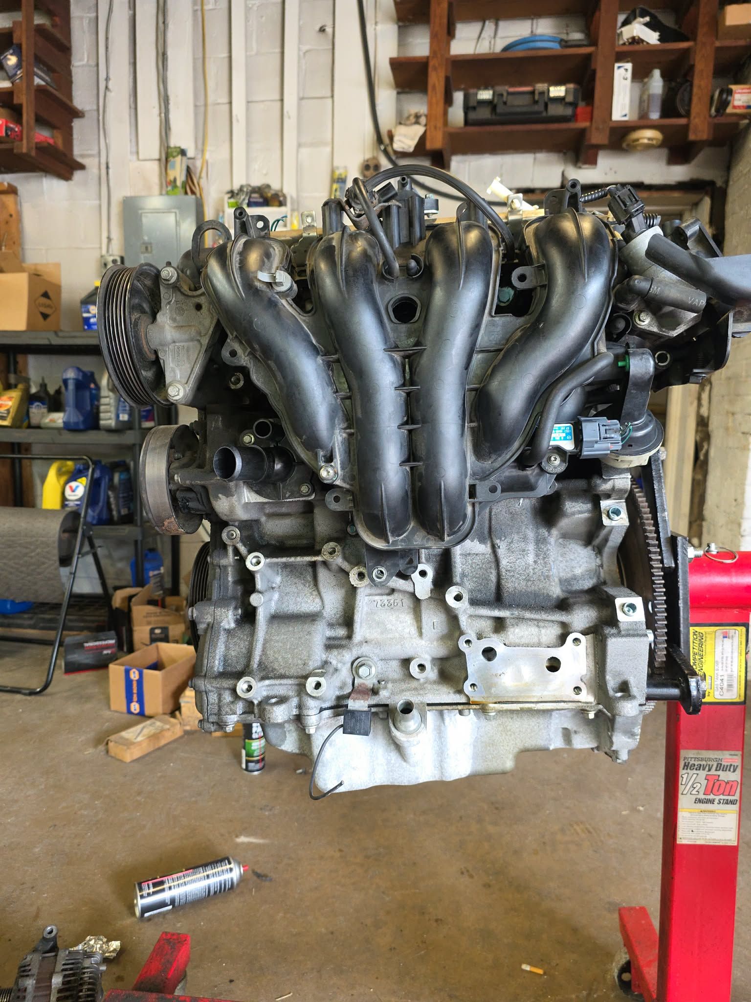 Engine assembly mounted on a red stand in a workshop, with black intake manifold and various parts visible. | Seth's Auto Care