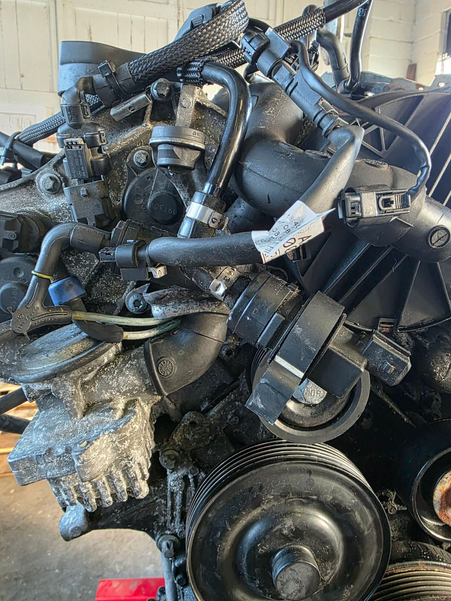 Black car engine with various hoses, belts, and pulleys; workshop setting, light background. | Seth's Auto Care