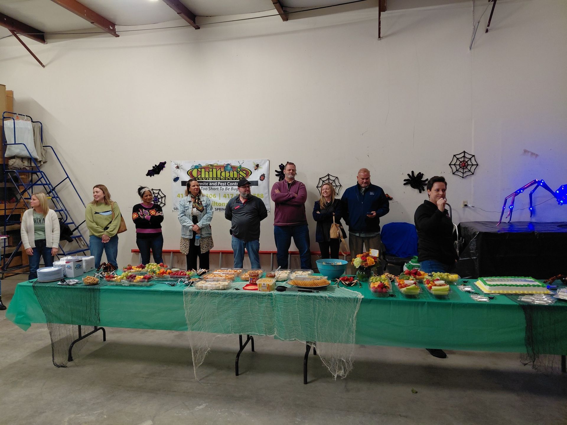 People at a buffet table, snacks laid out, Halloween decorations in a warehouse setting.