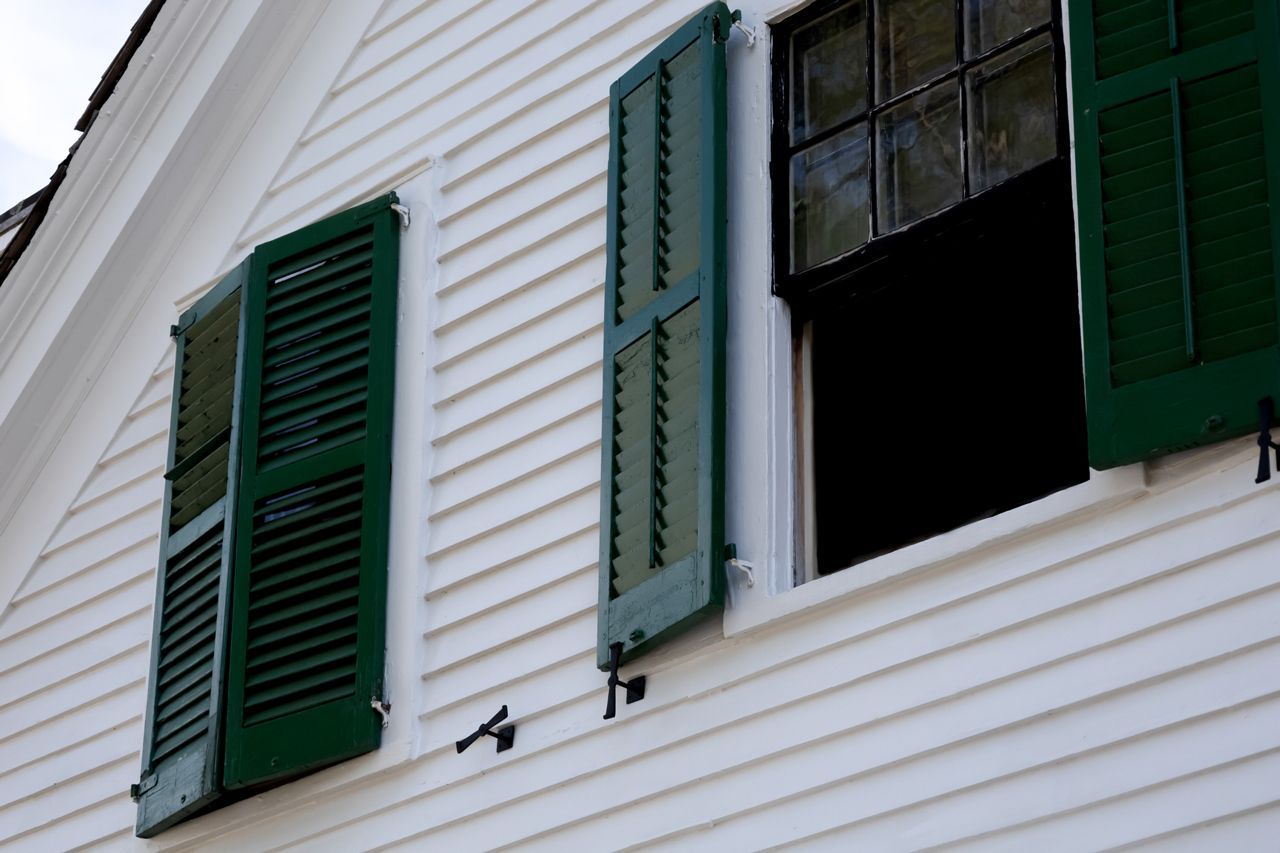 A white house with green shutters on the windows.