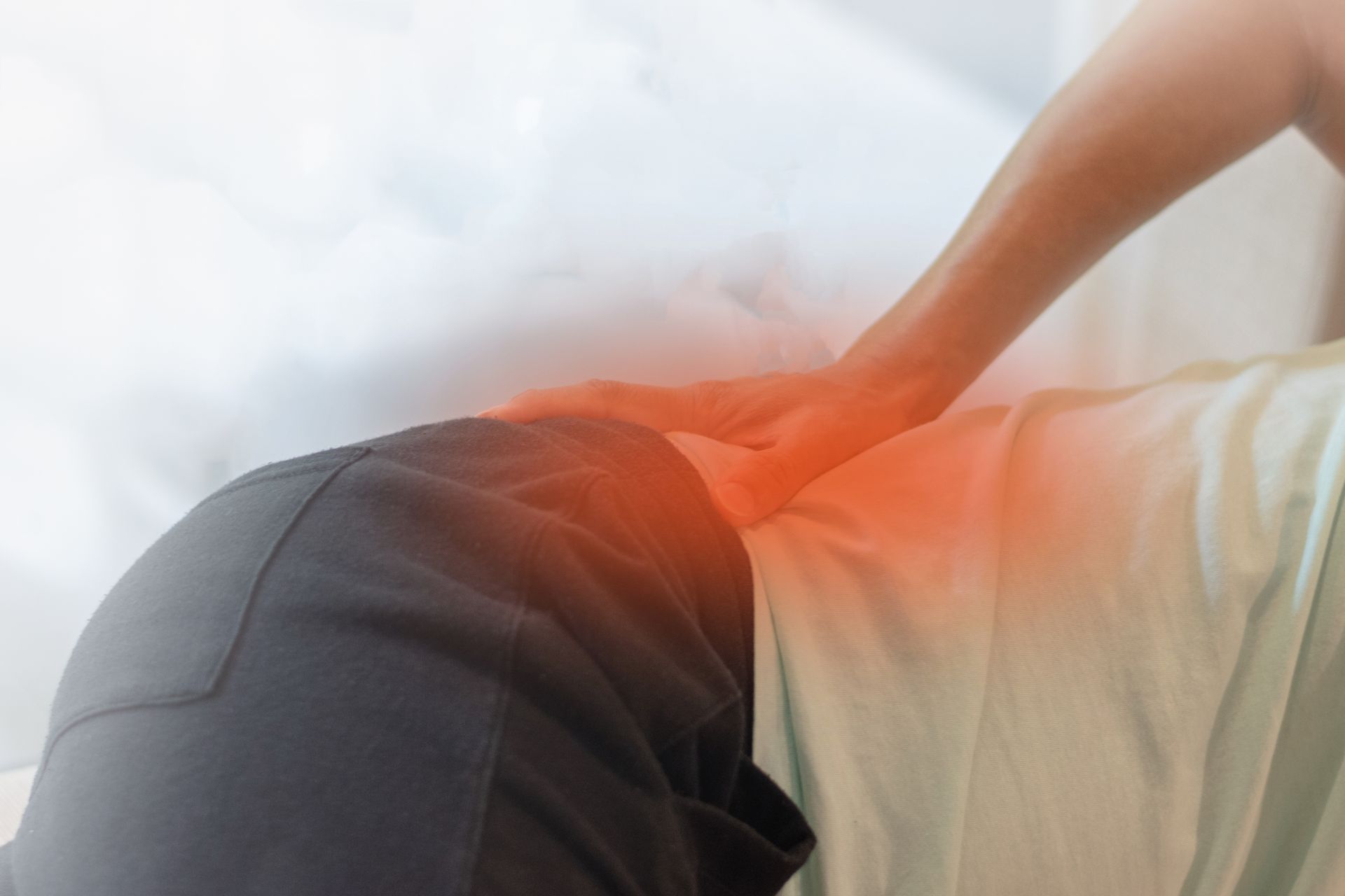 A person is laying on a bed holding their back in pain.