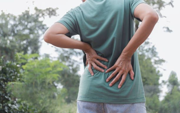 A man in a green shirt is holding his back in pain.