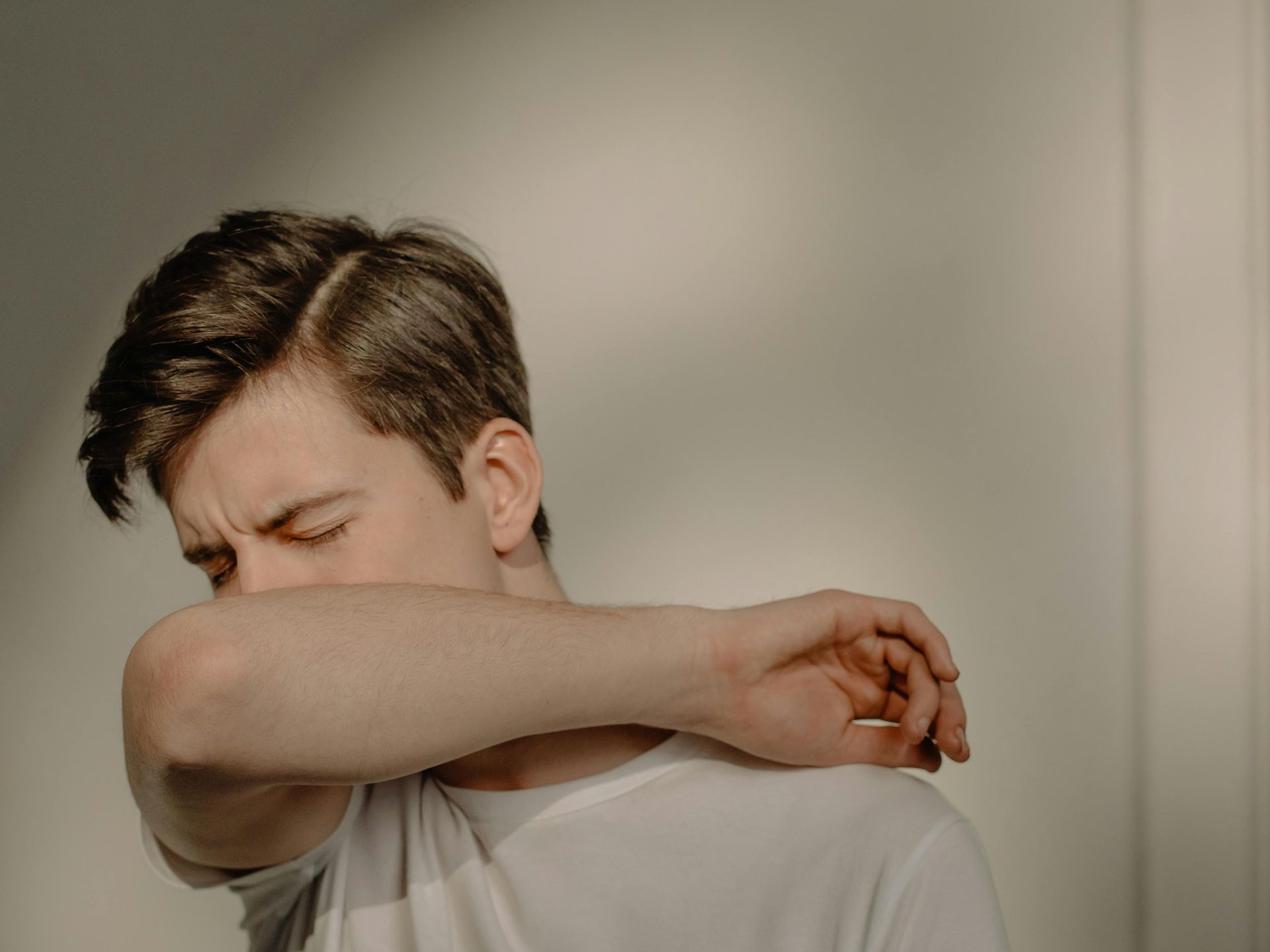 A young man is coughing into his elbow.