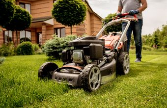 Person mowing a green lawn in front of a house with a push lawn mower