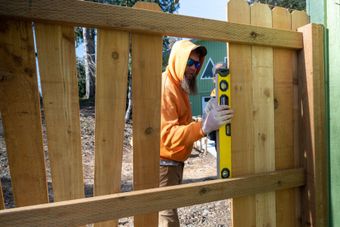 Person in an orange hoodie levels a wooden fence post with a spirit level.