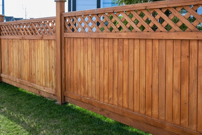 Wooden backyard fence with lattice top beside a green lawn.