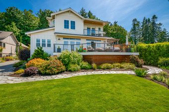 Modern two-story white house with a landscaped yard, patio, and large green lawn under a blue sky
