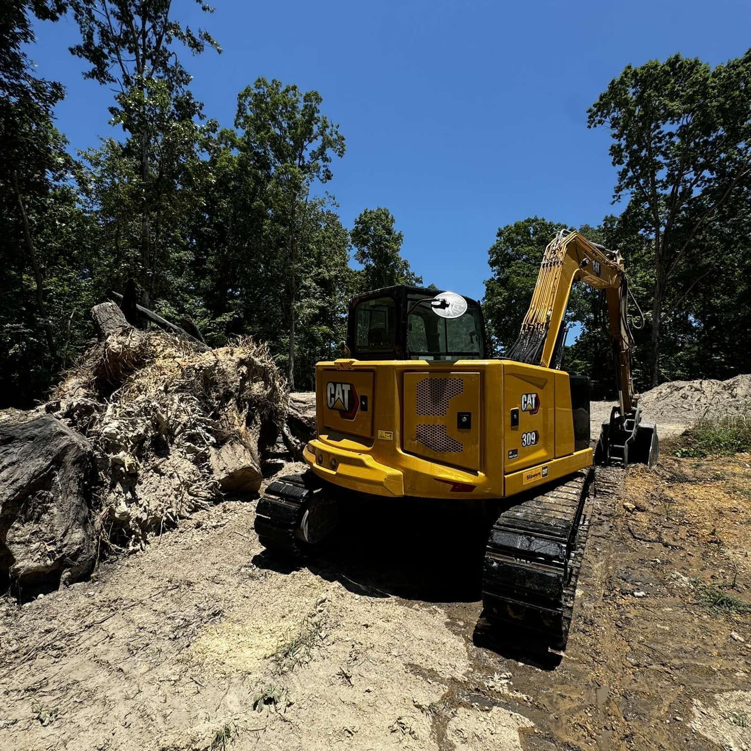 A yellow excavator is parked in front of a pile of trees