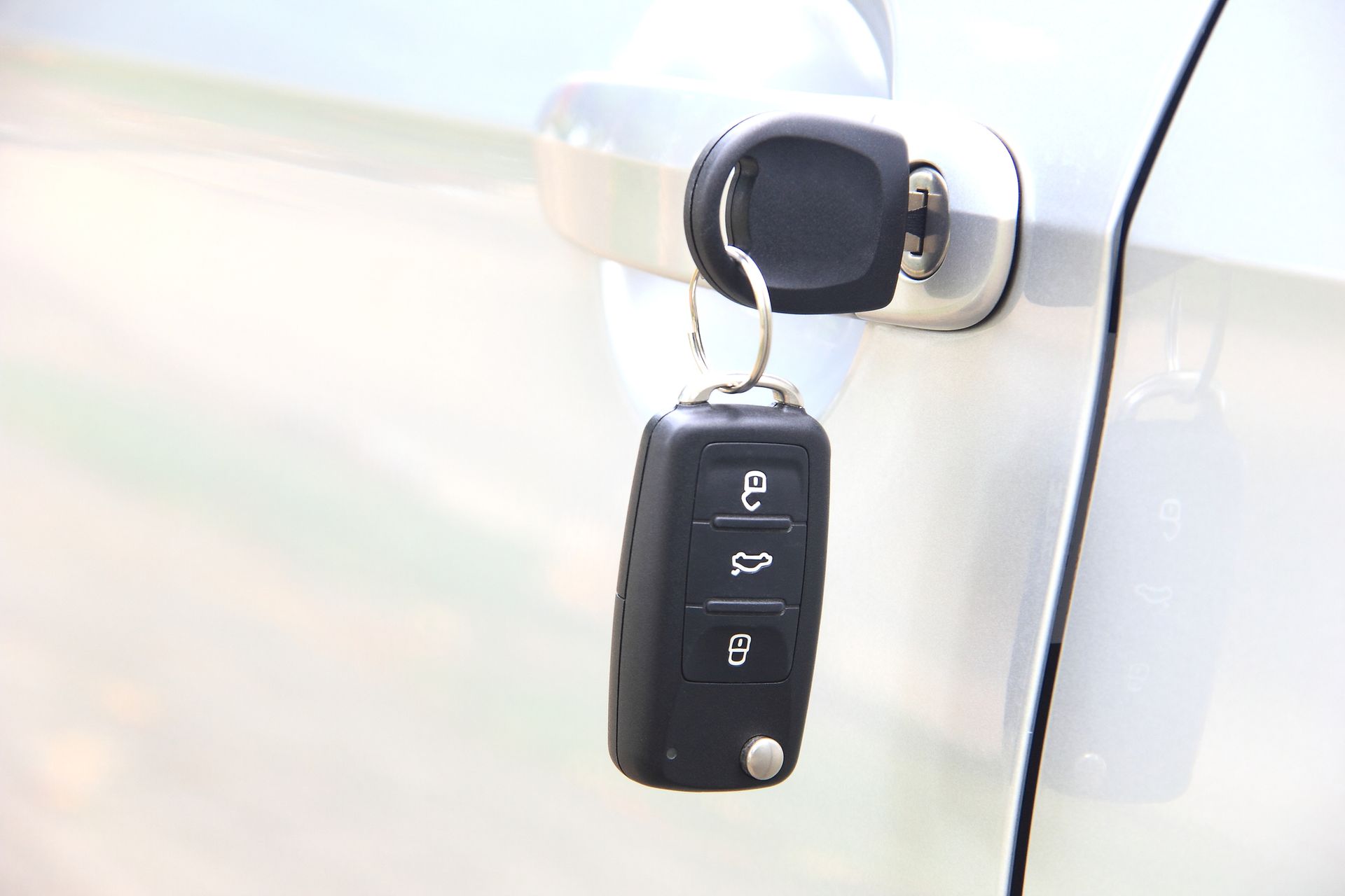 A car key is hanging from the door handle of a car.