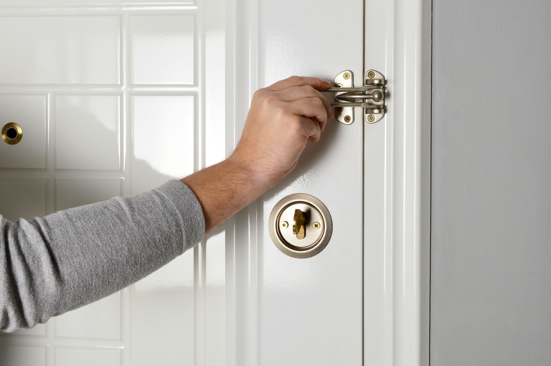 A person is holding a door latch on a white door.