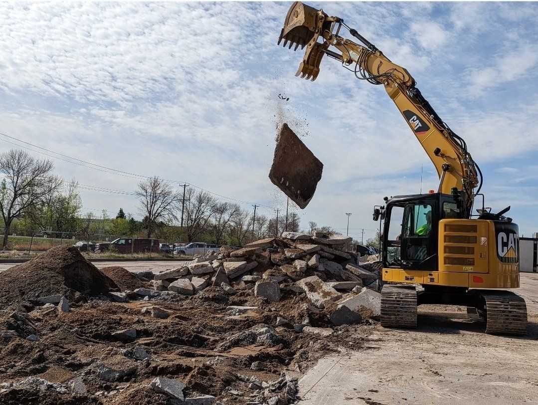 Large yellow excavator tearing up and moving old concrete. Rough CUts Construction.