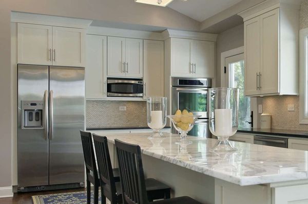 Kitchen with white cabinets, stainless steel appliances, marble island, and black bar stools.