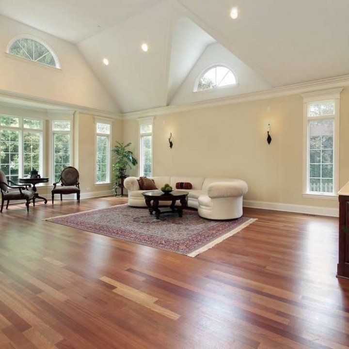 Spacious living room with hardwood floors, cream-colored walls, white couch on a patterned rug, and large windows.