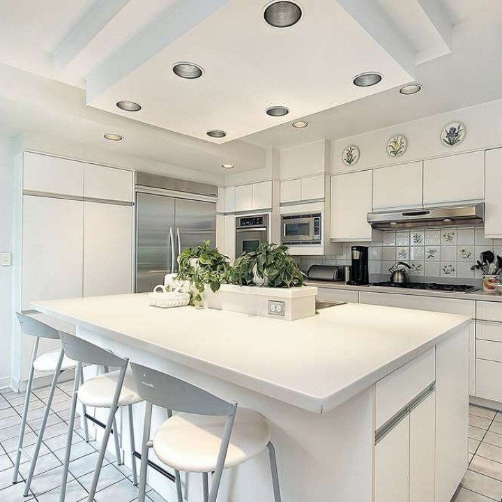 White kitchen with island and recessed lighting. Stainless steel appliances and plants.