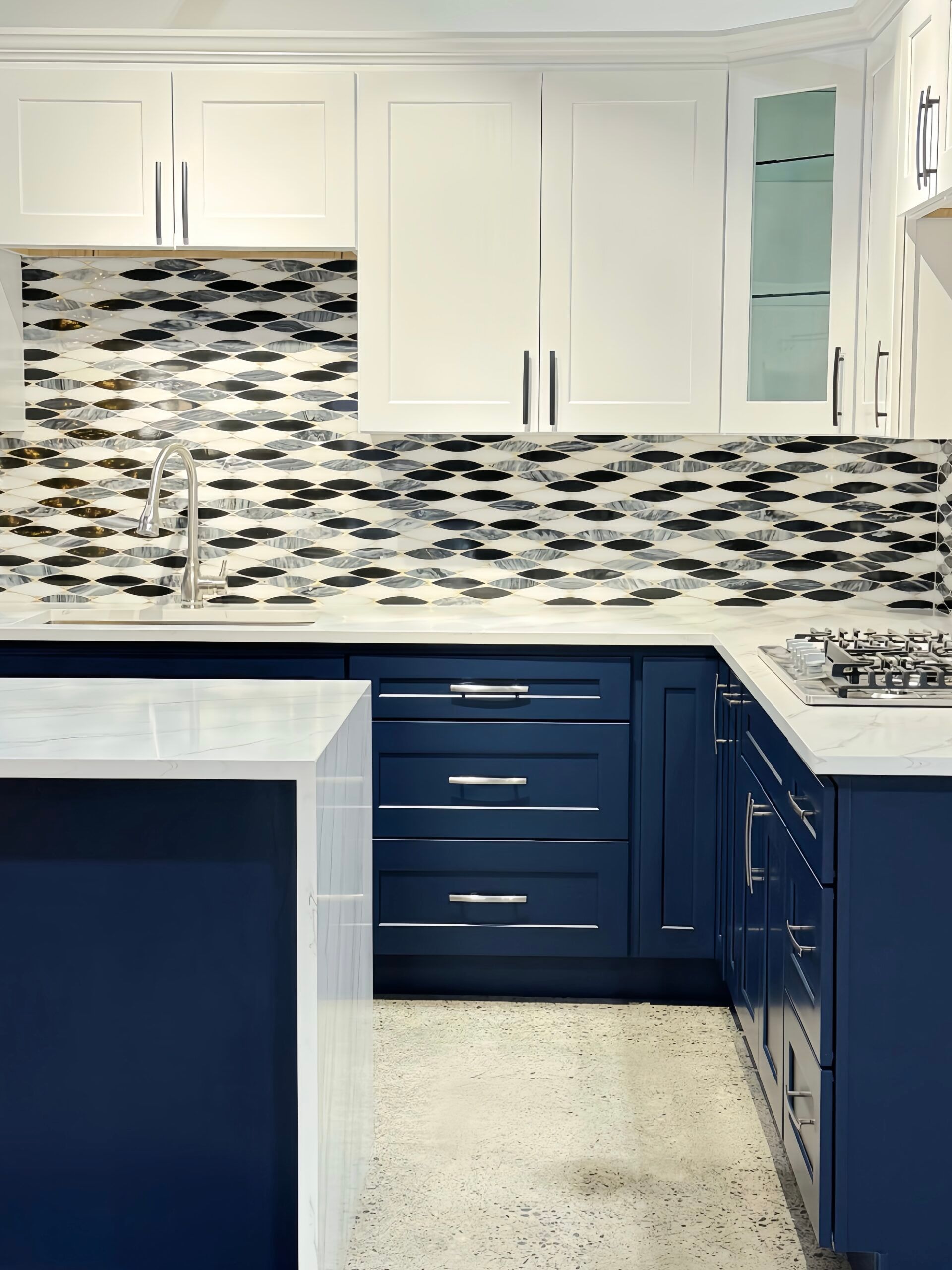 Navy blue and white kitchen with patterned backsplash, white countertops, and stainless steel hardware.
