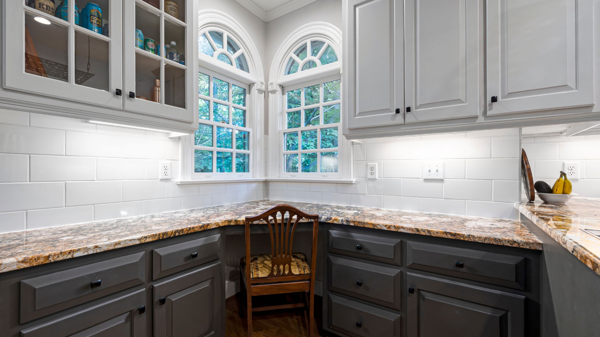 Gray and white kitchen with cabinets, countertops, and two arched windows.