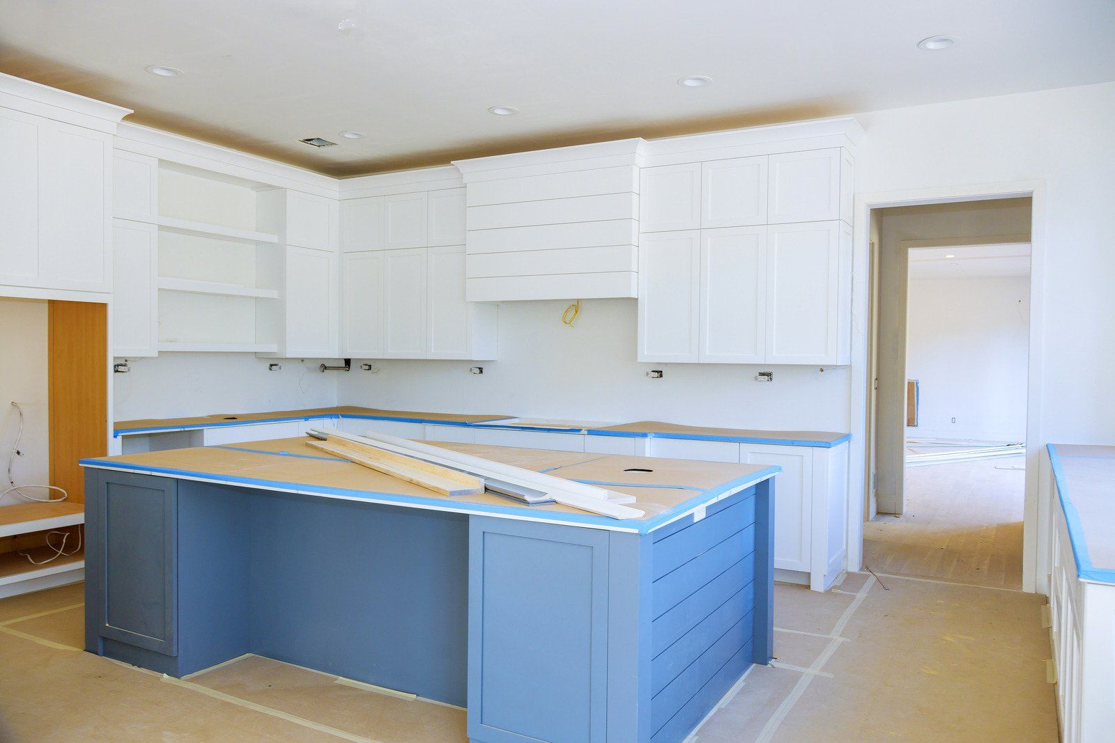 Kitchen undergoing renovation; white cabinets, blue island, unfinished countertops, doorway.