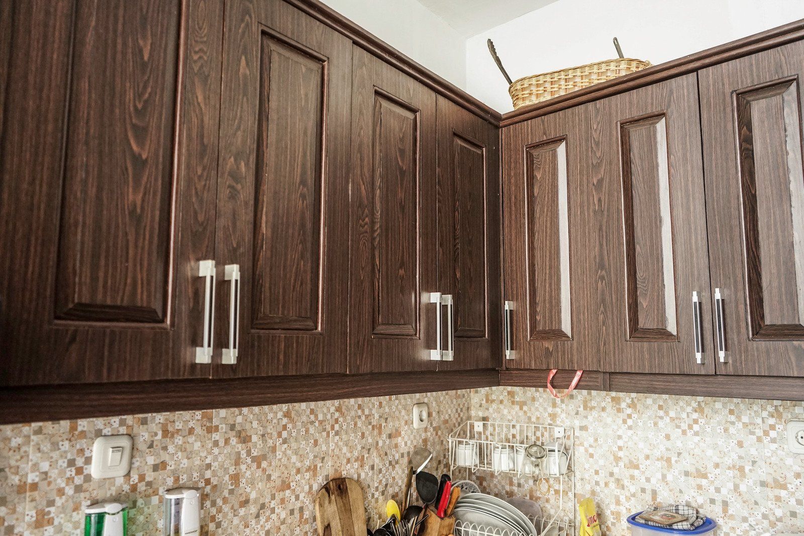 Dark wood kitchen cabinets with silver handles above a mosaic tile backsplash.