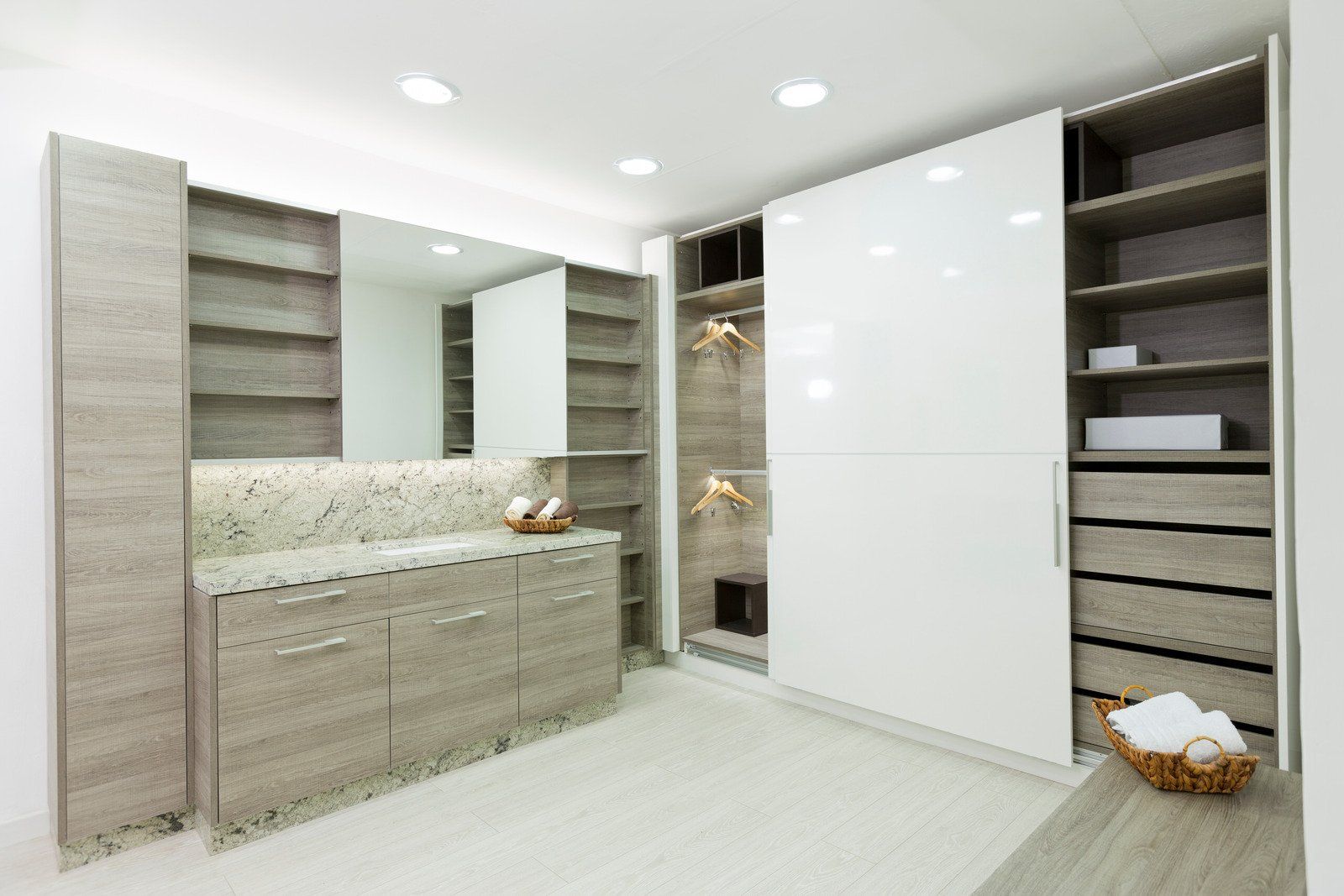 A bright, modern walk-in closet with white and light wood cabinetry, shelving, and drawers.