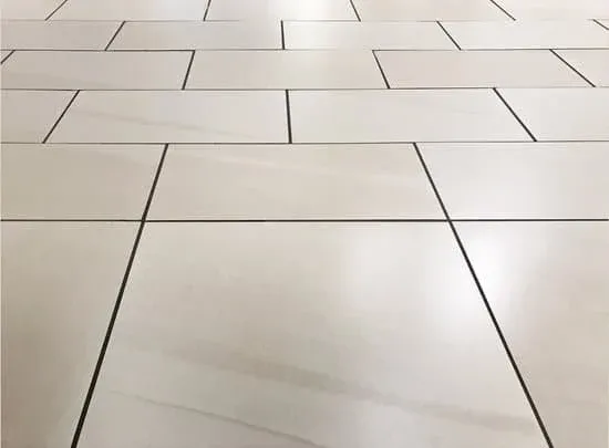 Cream-colored rectangular tiles with dark grout lines, laid in a repeating pattern, covering a floor.