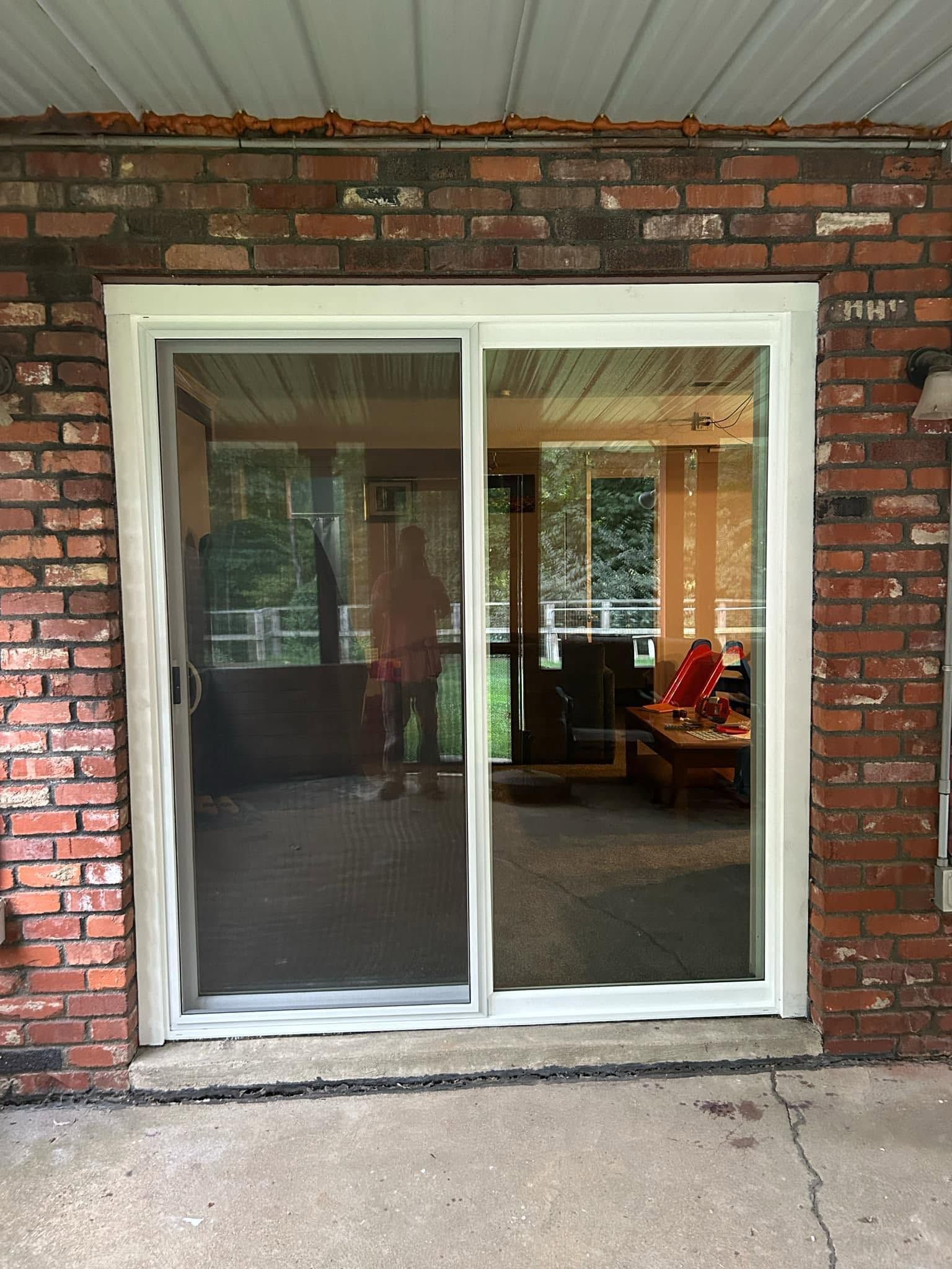 Sliding glass door in a red brick wall, with a screened panel and interior visible behind it
