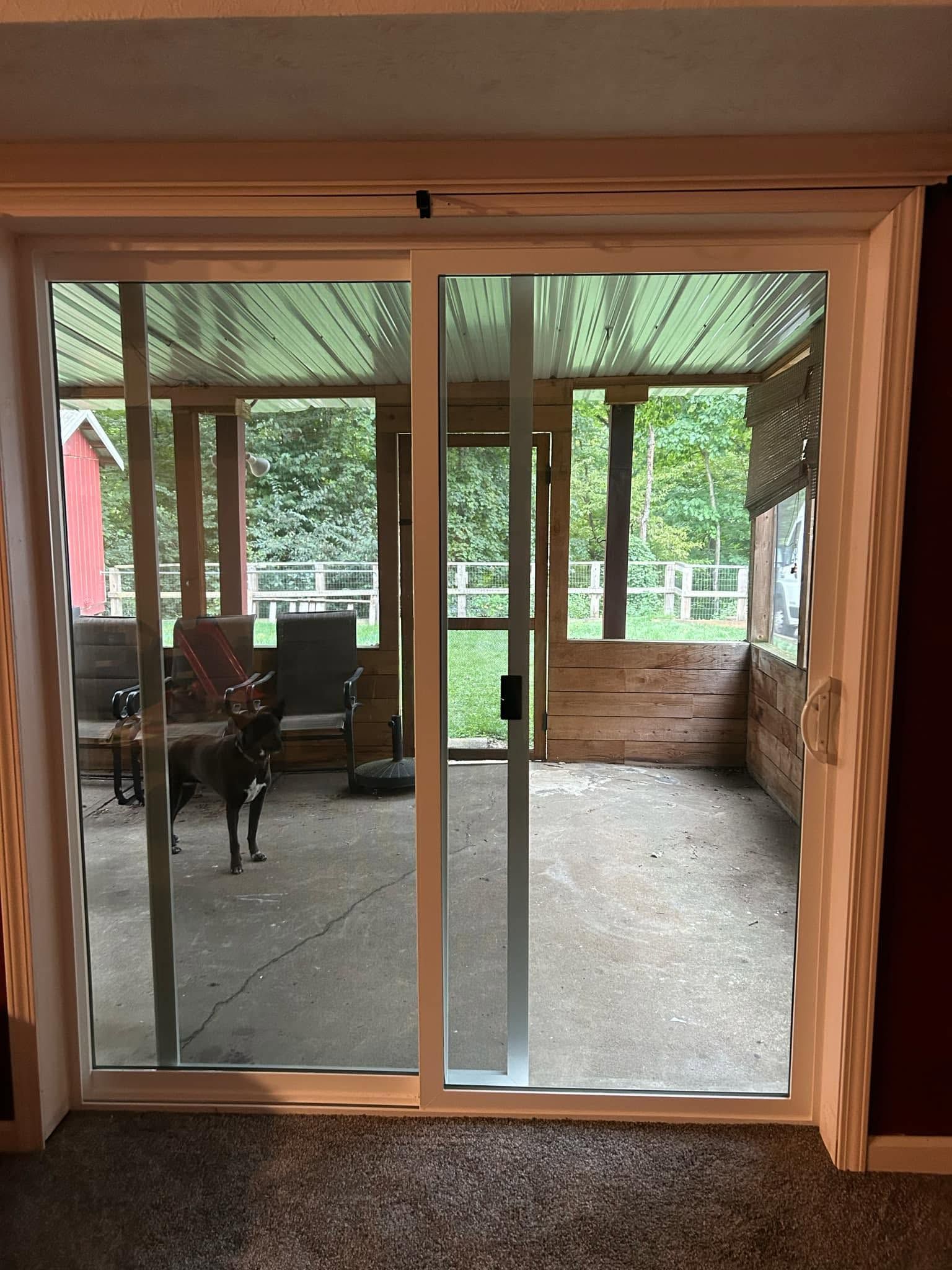 Glass sliding doors opening to a covered patio with outdoor furniture and a dog inside.