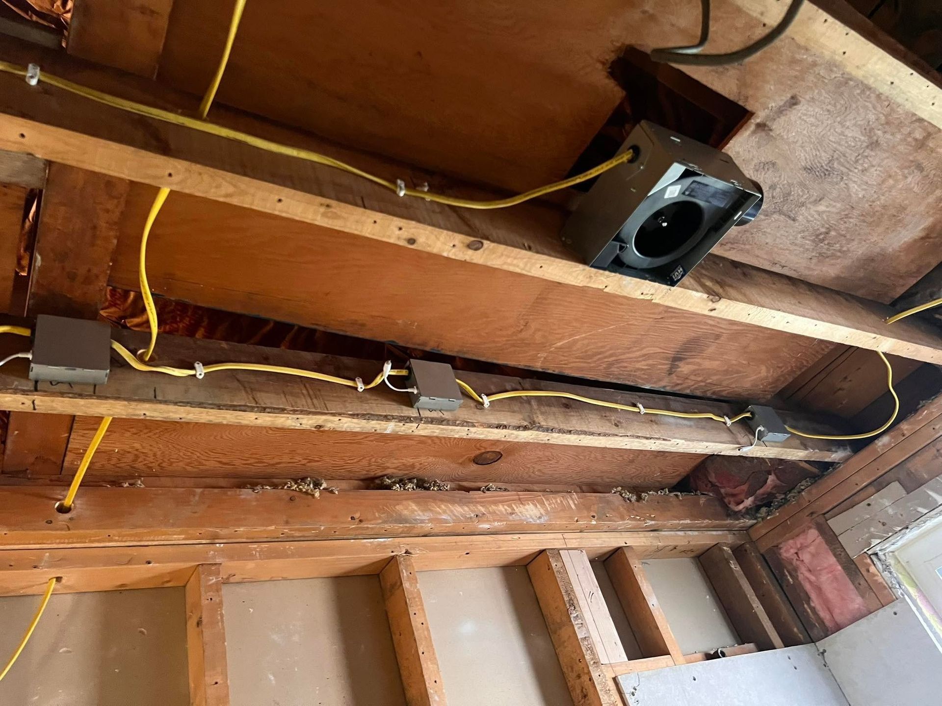 Exposed wooden ceiling joists with yellow electrical wires and a black speaker or vent opening.